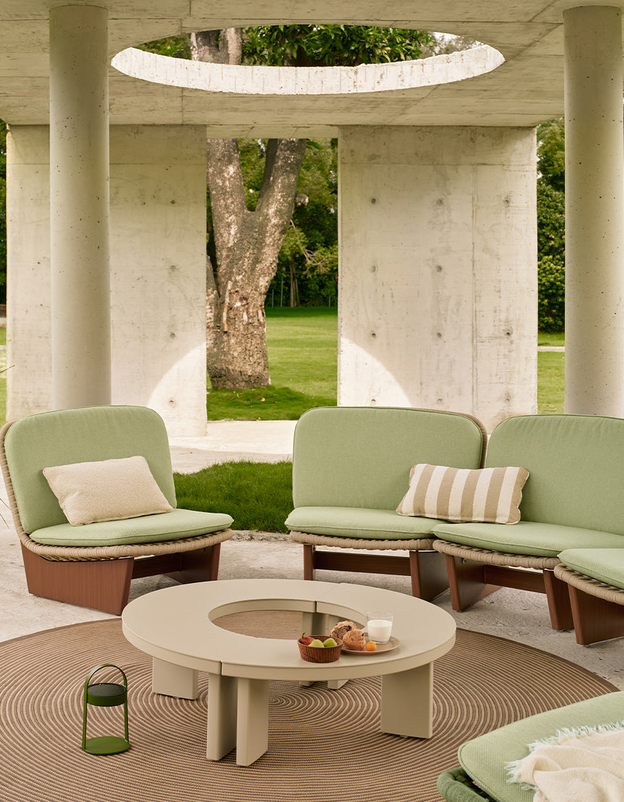 Outdoor seating area with green sofas and a round table in a modern architectural setting.